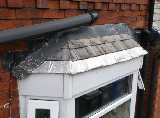 Slated and hipped bay window roof, heavily deteriorated, with rudimentary flash-band repairs to the flashing and first row of slating.