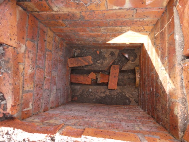 View within an inspection chamber, showing brickwork lying in the underground drainage following internal collapse of the top course.