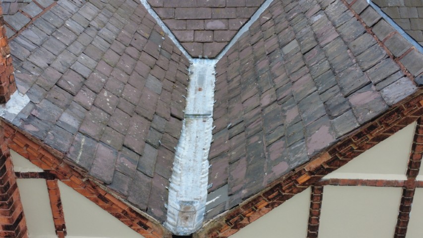 Inverted valley and central gully detail with adjacent roof coverings significantly deteriorated, showing extensive historical repair.