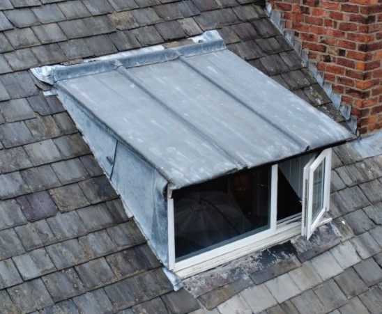 Lead sheet-covered dormer, severely deteriorated and distorted, with debris build-up in the back gutter, at the end of its serviceable life.