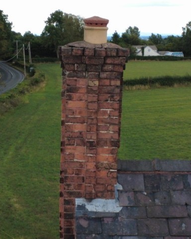 A brick-built chimney stack on an early 19th-century farmhouse, leaning significantly out of vertical and requiring structural intervention.